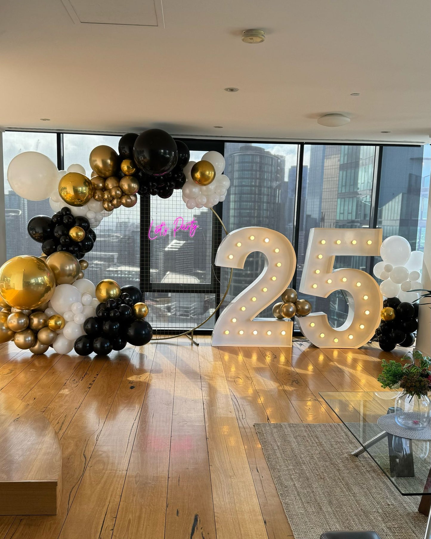 25th birthday celebration in Southbank apartment with a Lets Party neon and black gold and white balloon garland against a window of Southbank skyline