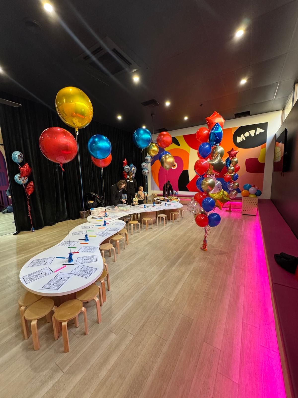 Colorful balloon display in a room with tables and chairs, featuring a 'Mova' sign.