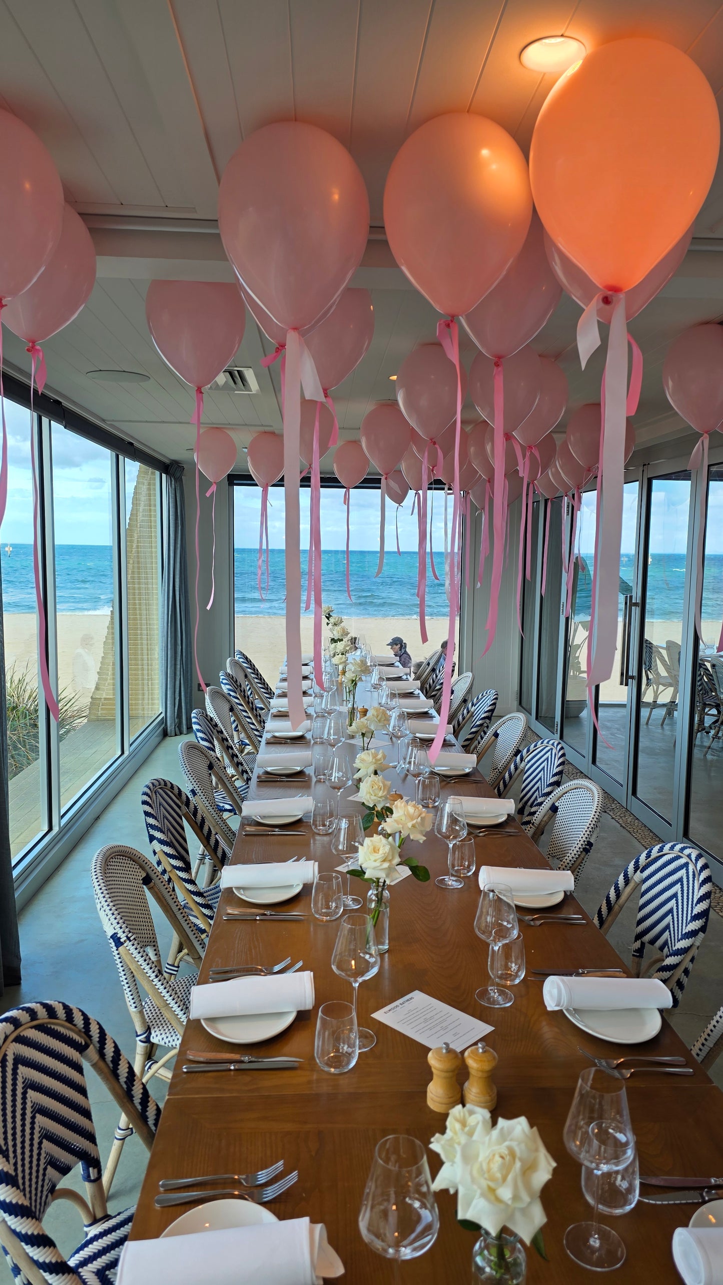 Dining table set for a formal event with pink balloons, white flowers at the Elwood bathers pavilion 