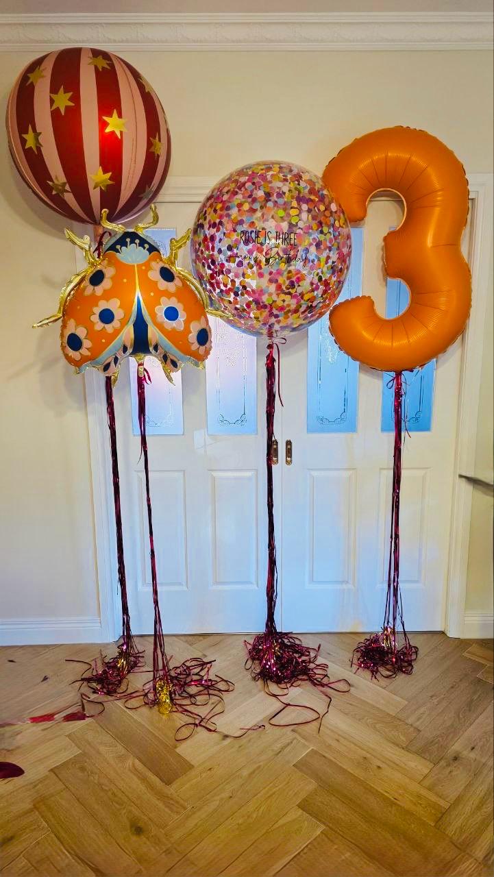 Colorful balloons including a number '3' and a ladybug design on a wooden floor.