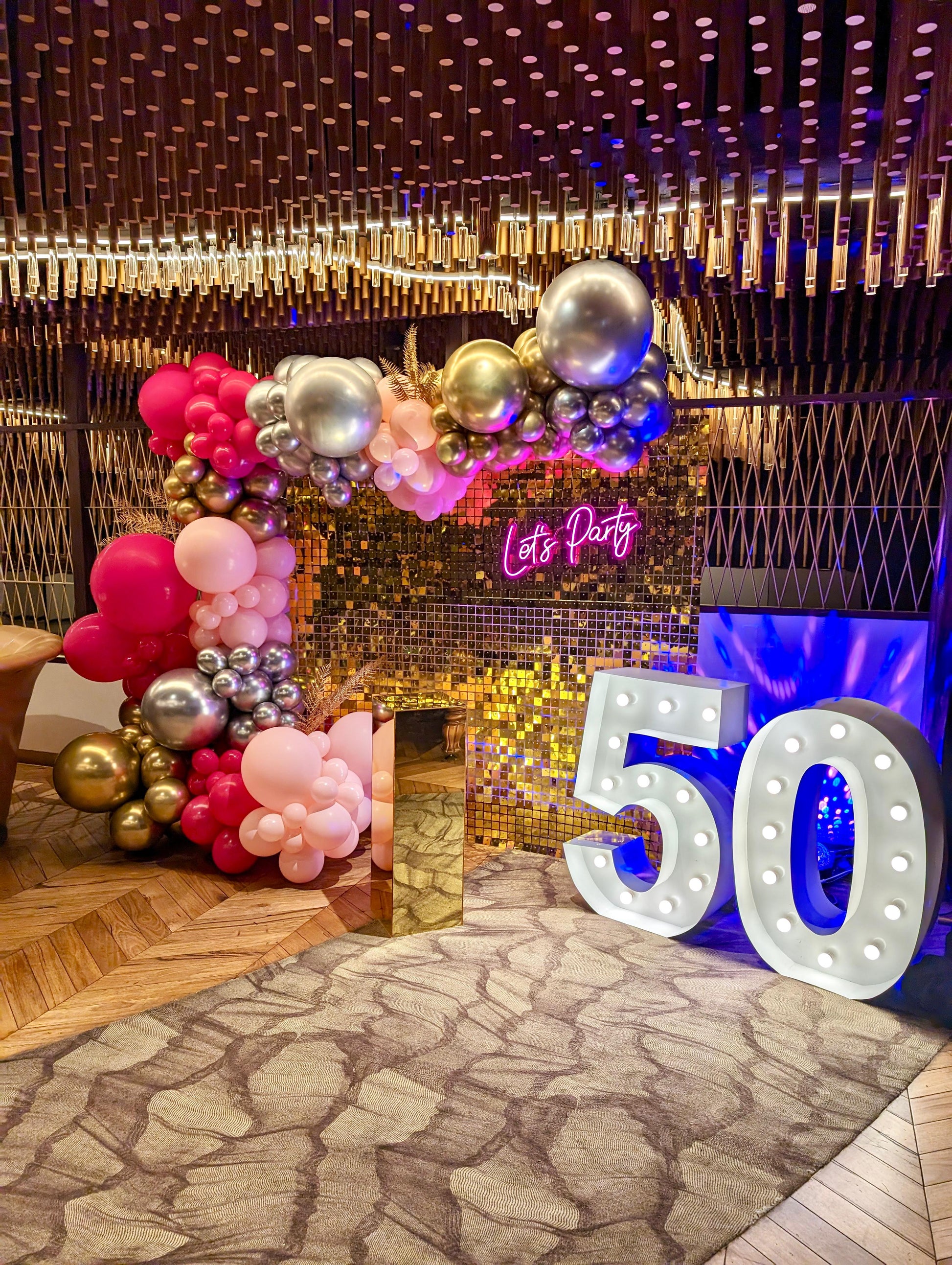 Hot Pink and Silver Balloon Garland with a "50" light up numbers sign, a "lets party" sign and a gold plinth