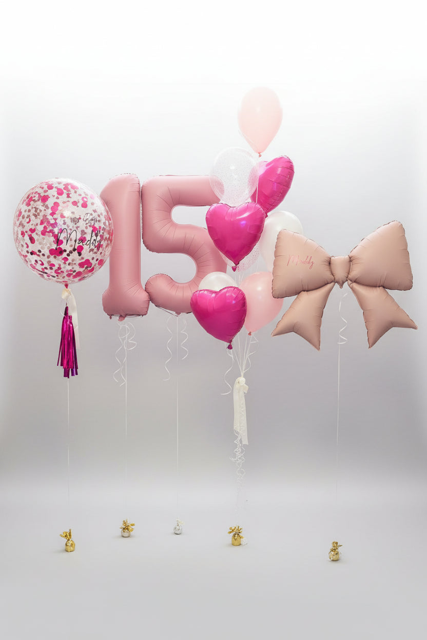 Decorative balloons with numbers and letters, including a large pink number '15', heart shapes, and a bow, against a floral wallpapered wall.