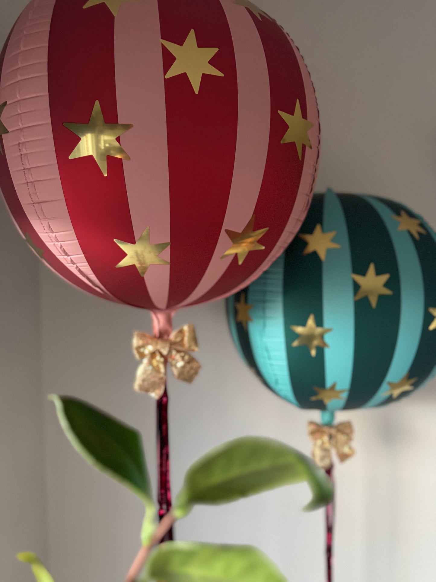 Decorative balloons with red and blue stripes and gold stars, tied with ribbons, against a neutral background.
