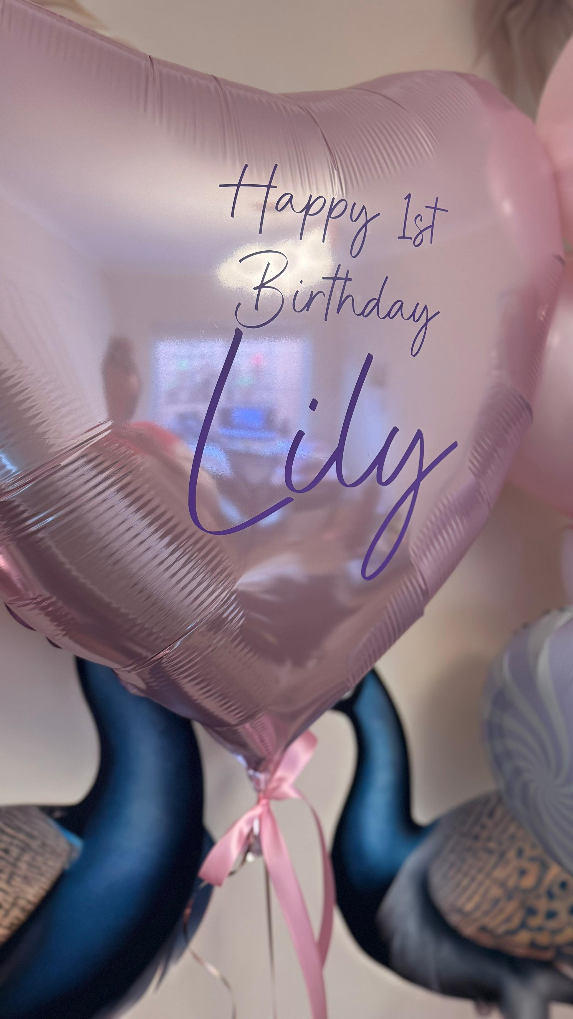 Pink balloon with 'Happy 1st Birthday Lily' text, held by a person.
