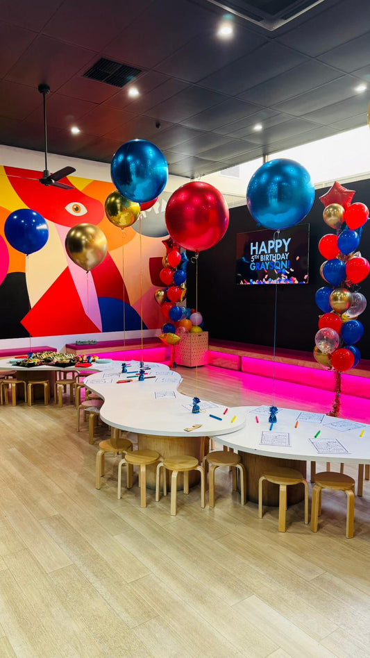 Children's play area with colorful balloons, tables, and chairs in a modern indoor setting.