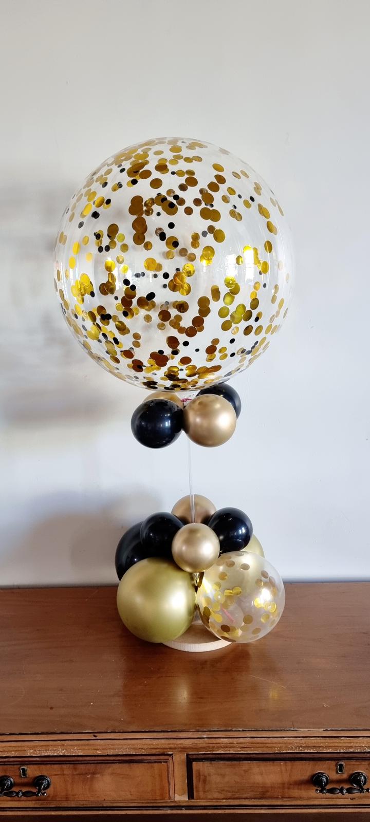 Decorative balloons with gold and black confetti on a wooden surface.