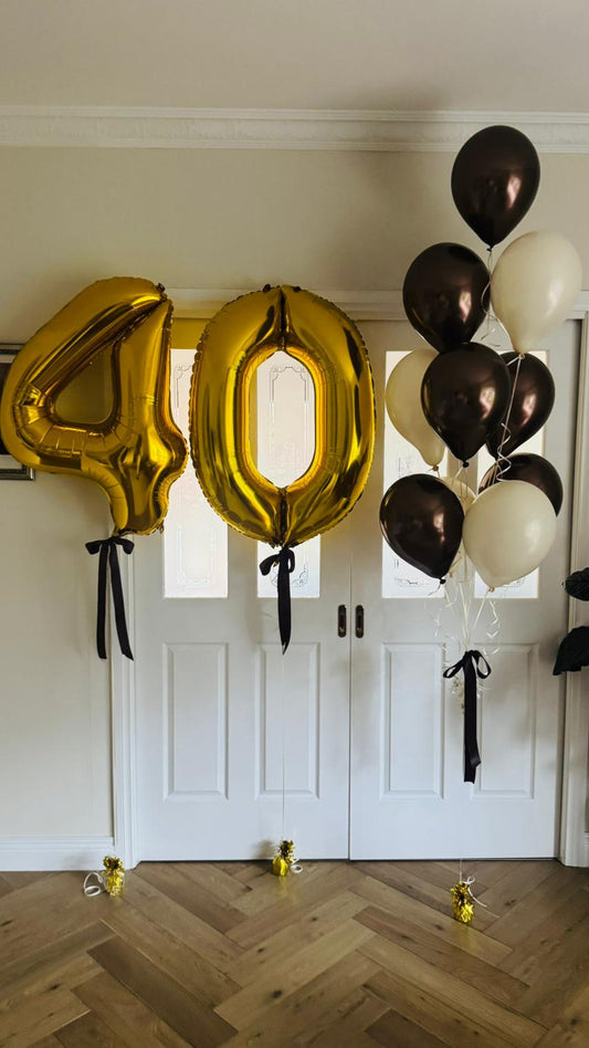 Gold '40' balloons and brown and vanilla white balloons against a white door.