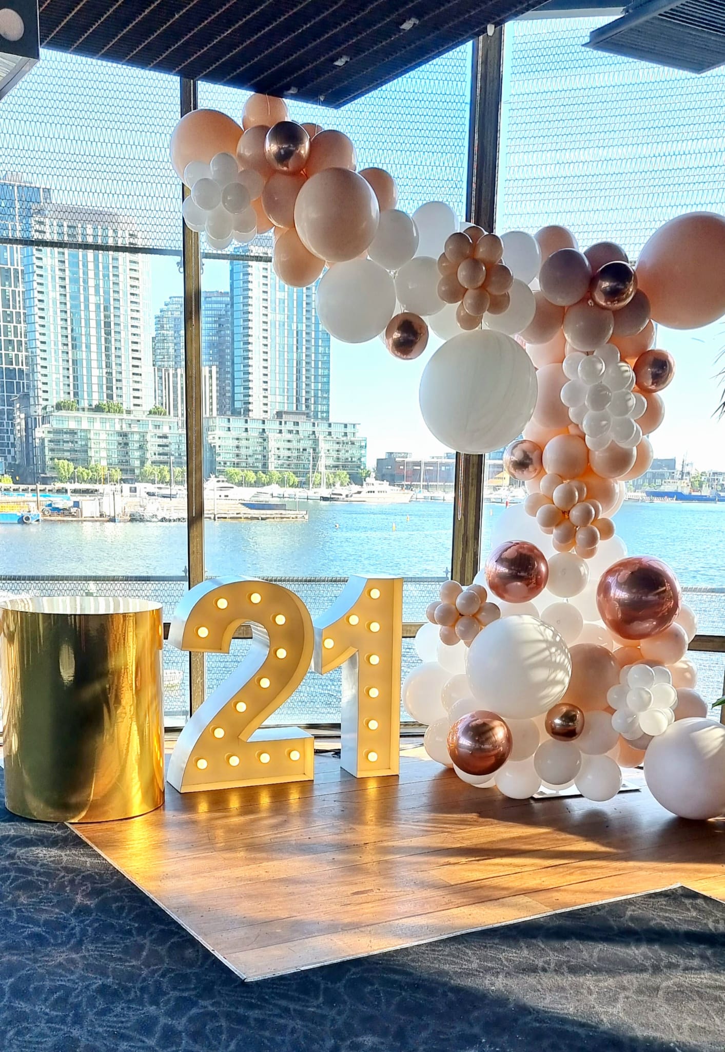 A balloon garland featuring round balloons in white, gold, and blush colors, with a large number '21' in the foreground.
