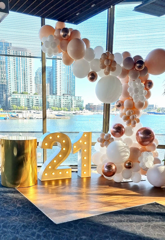 A balloon garland featuring round balloons in white, gold, and blush colors, with a large number '21' in the foreground.