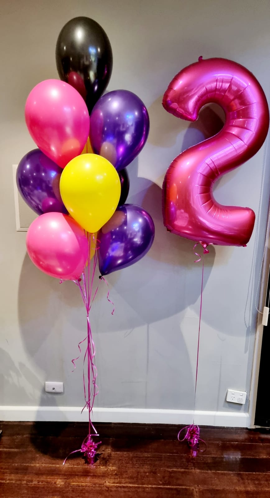 A bouquet of pink, purple, and yellow foil and latex balloons shaped as numbers '21' and 'W' for 'The Wiggles' themed party decorations.